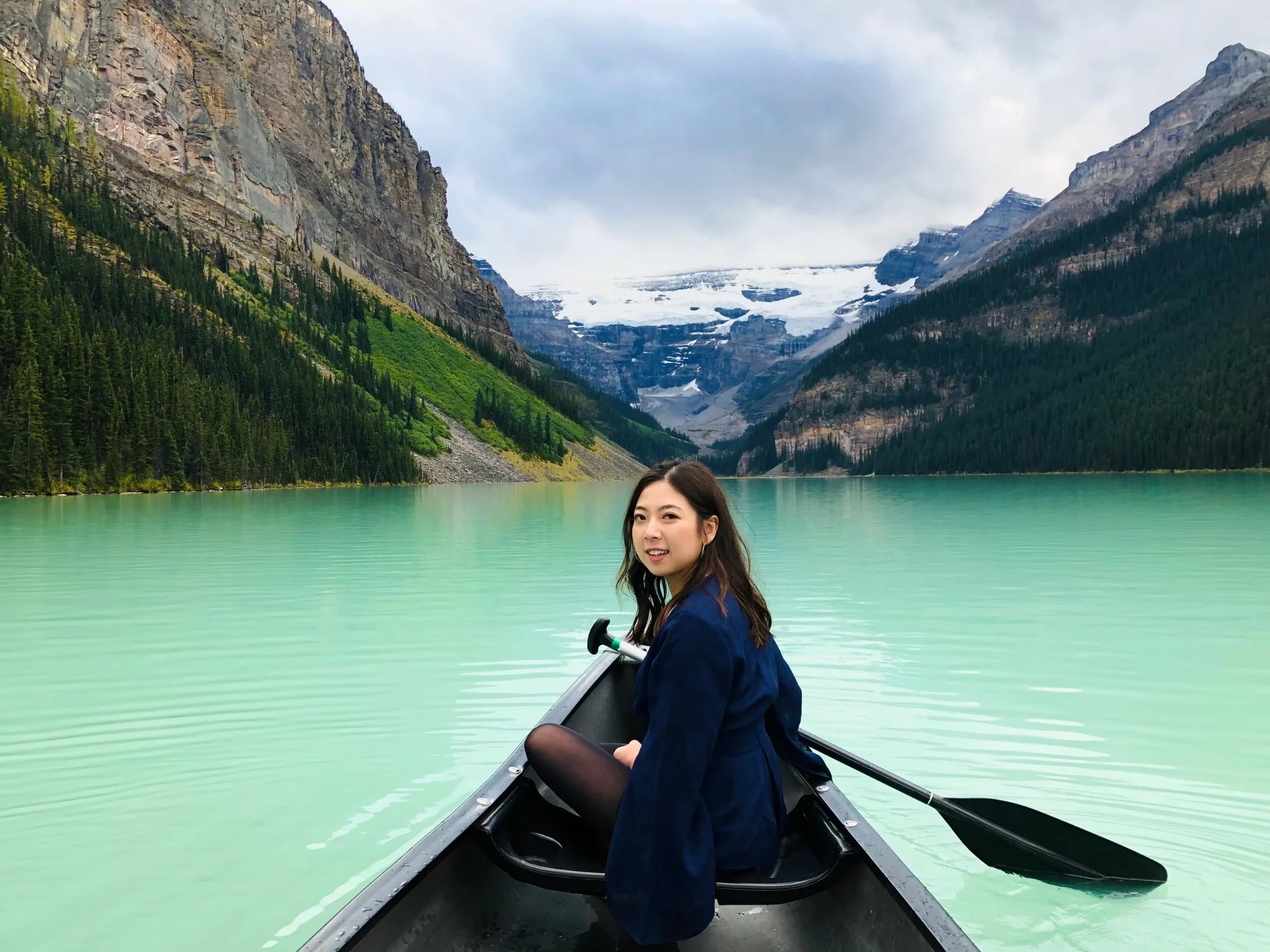 Agnes smiling over her shoulder from a canoe on a turquoise mountain lake