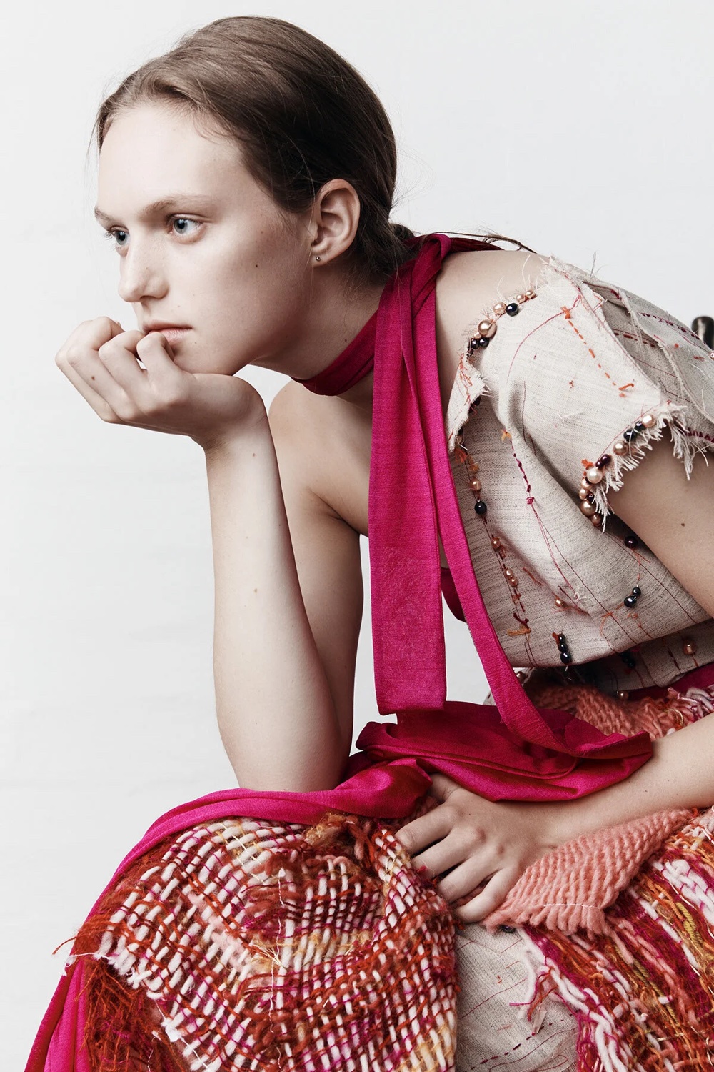 Model seated on a chair in a pale pink top with a red woven skirt